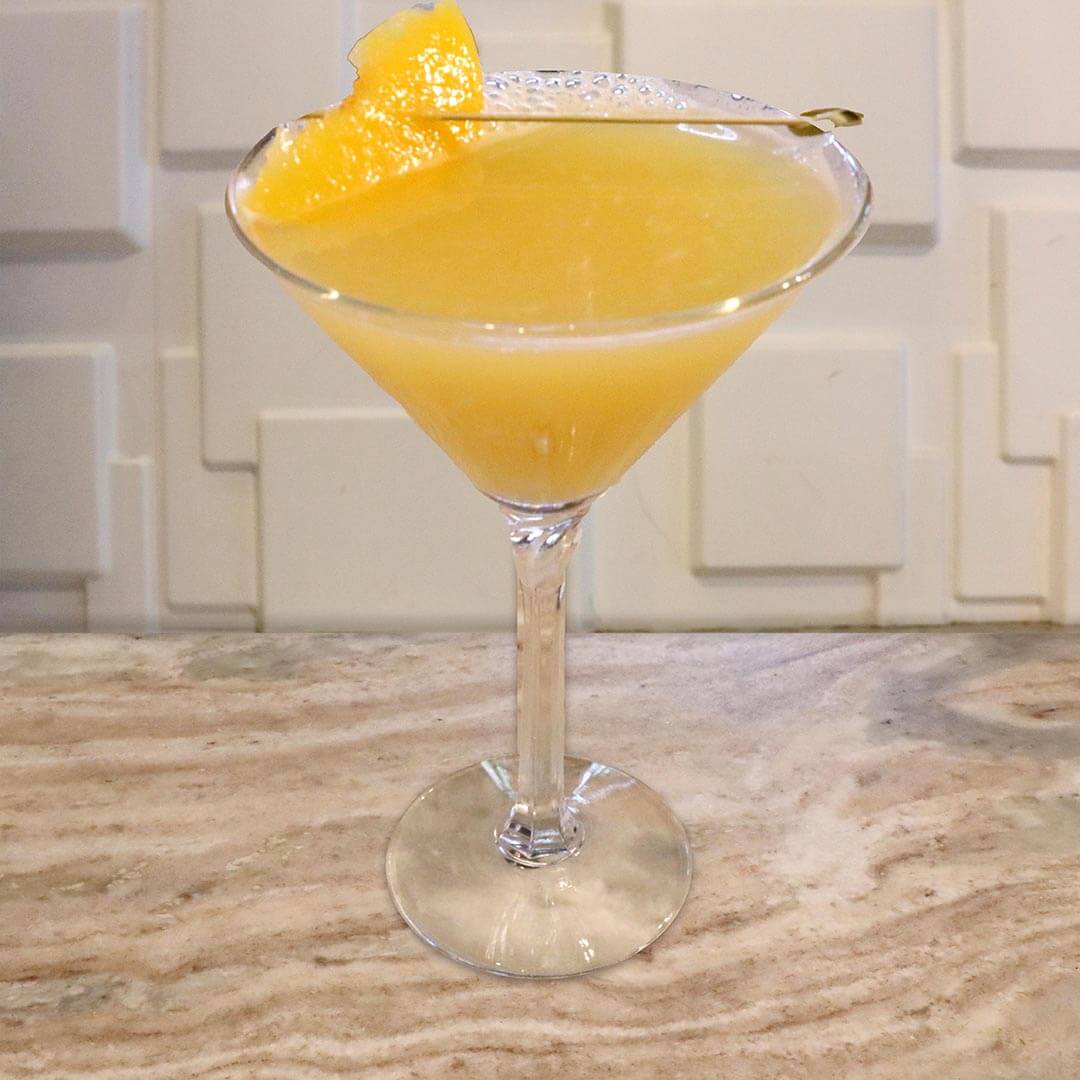 A soft yellow tropical cocktail served in a chilled glass, garnished with a peach slice.