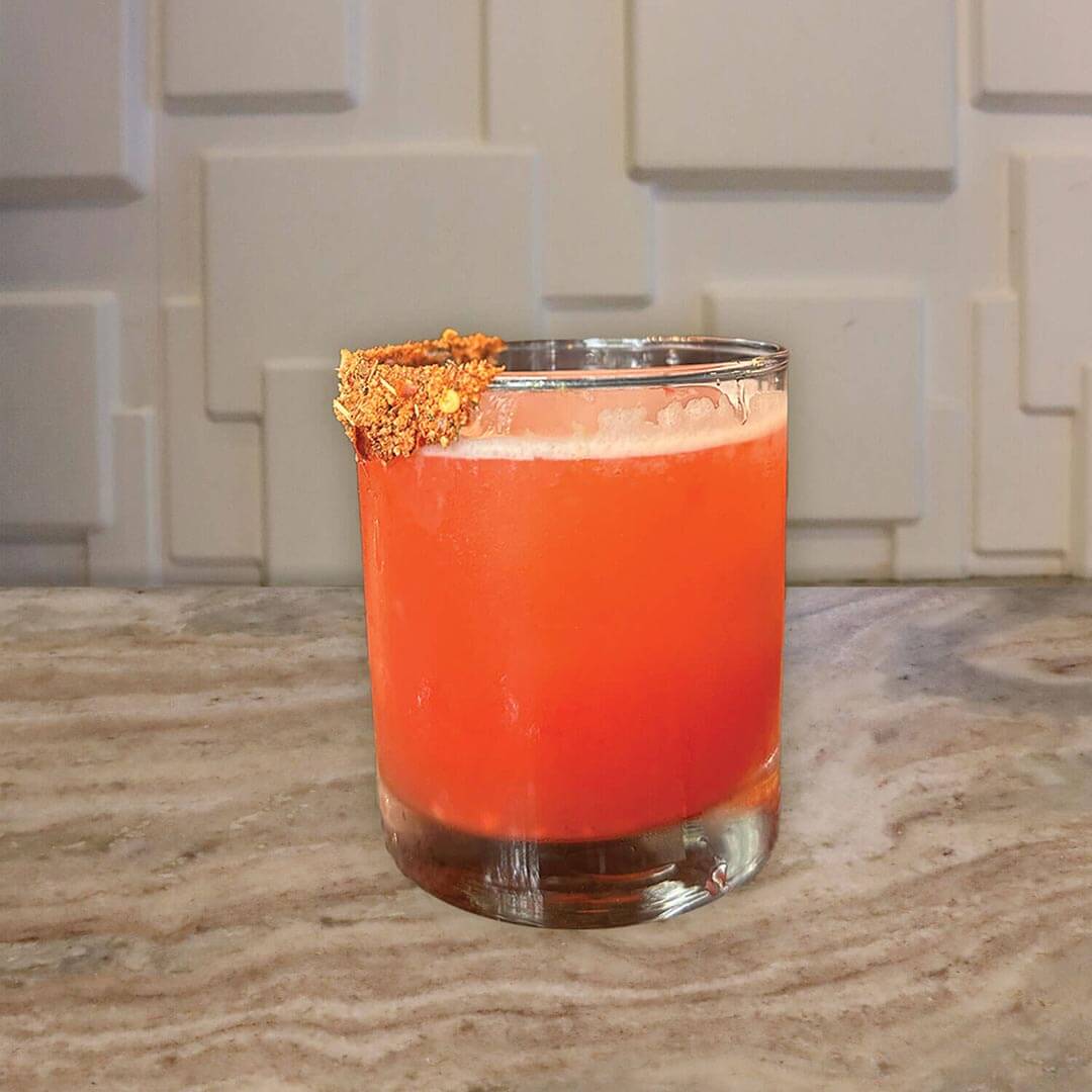 A vibrant orange-red beverage featuring a seasoned spicy rim.