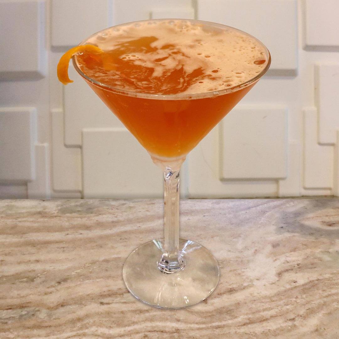 A bright orange citrus cocktail in a chilled glass, elegantly garnished with an orange peel.