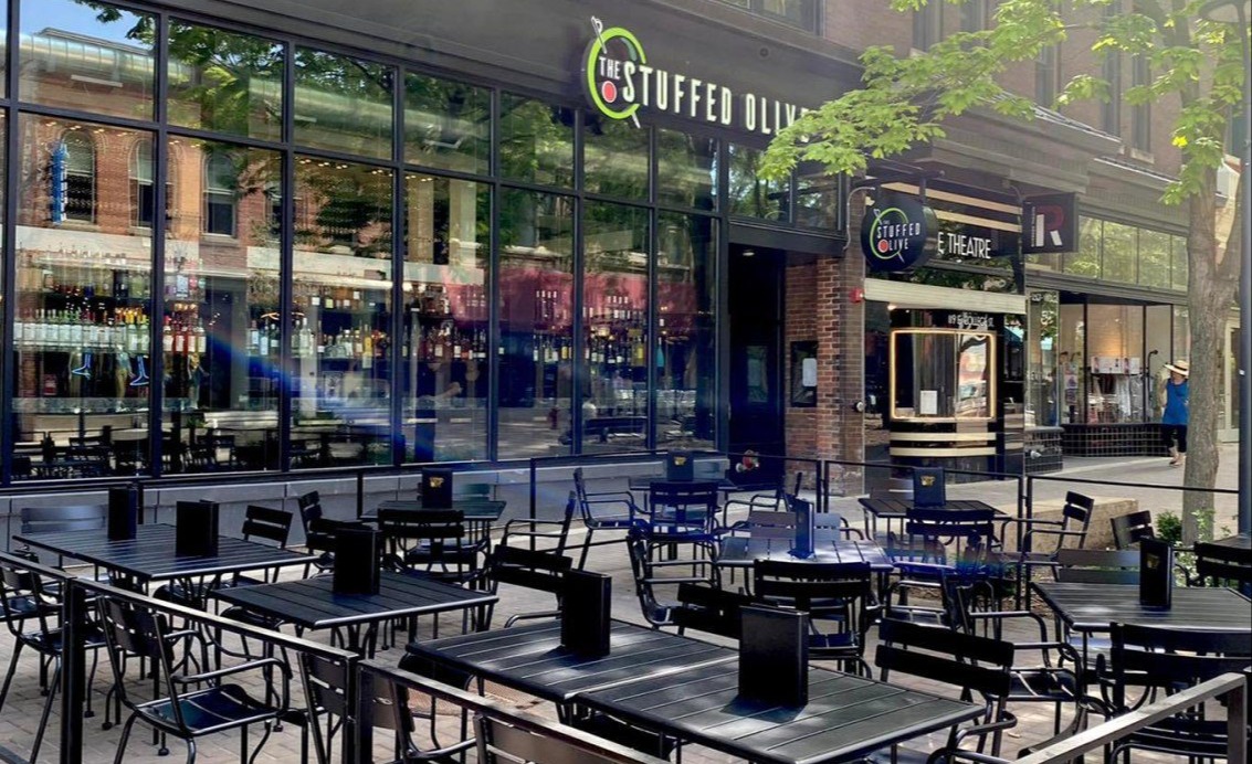 Street view of The Stuffed Olive exterior, showcasing large windows and an outdoor dining patio.