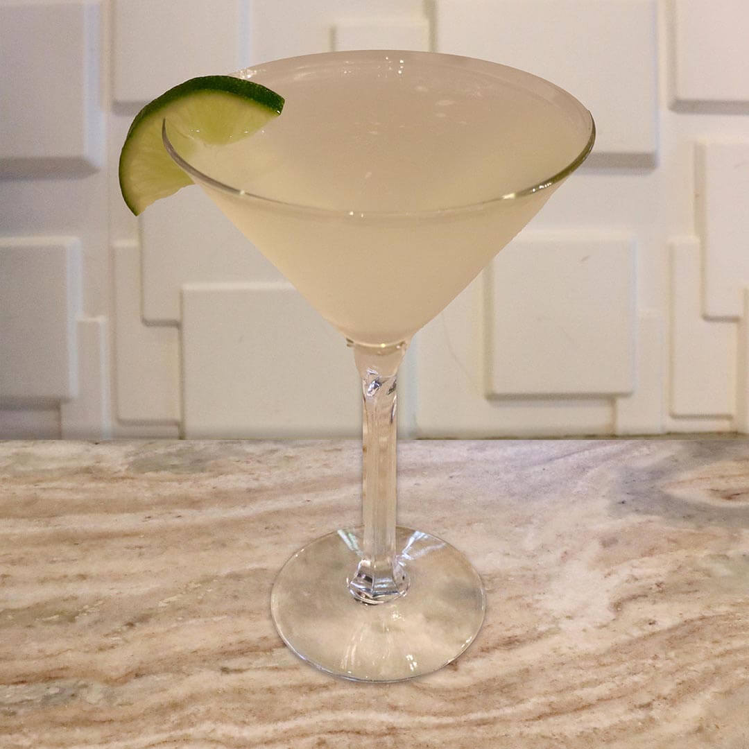 A translucent, pale green lime cocktail served in a chilled glass, garnished with a lime wheel.
