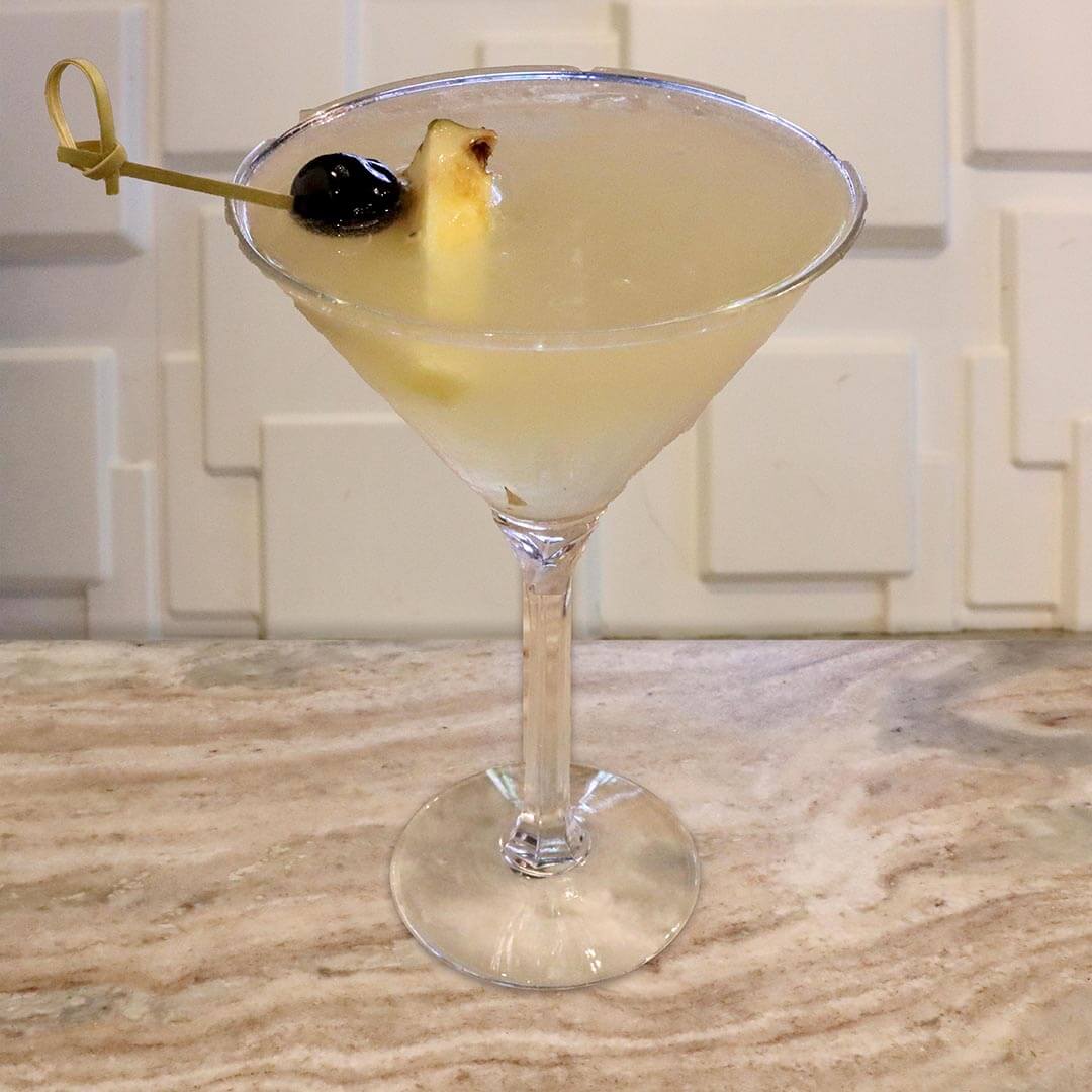 A yellow pineapple cocktail featuring a red cherry resting at the bottom of the glass and a lemon twist.