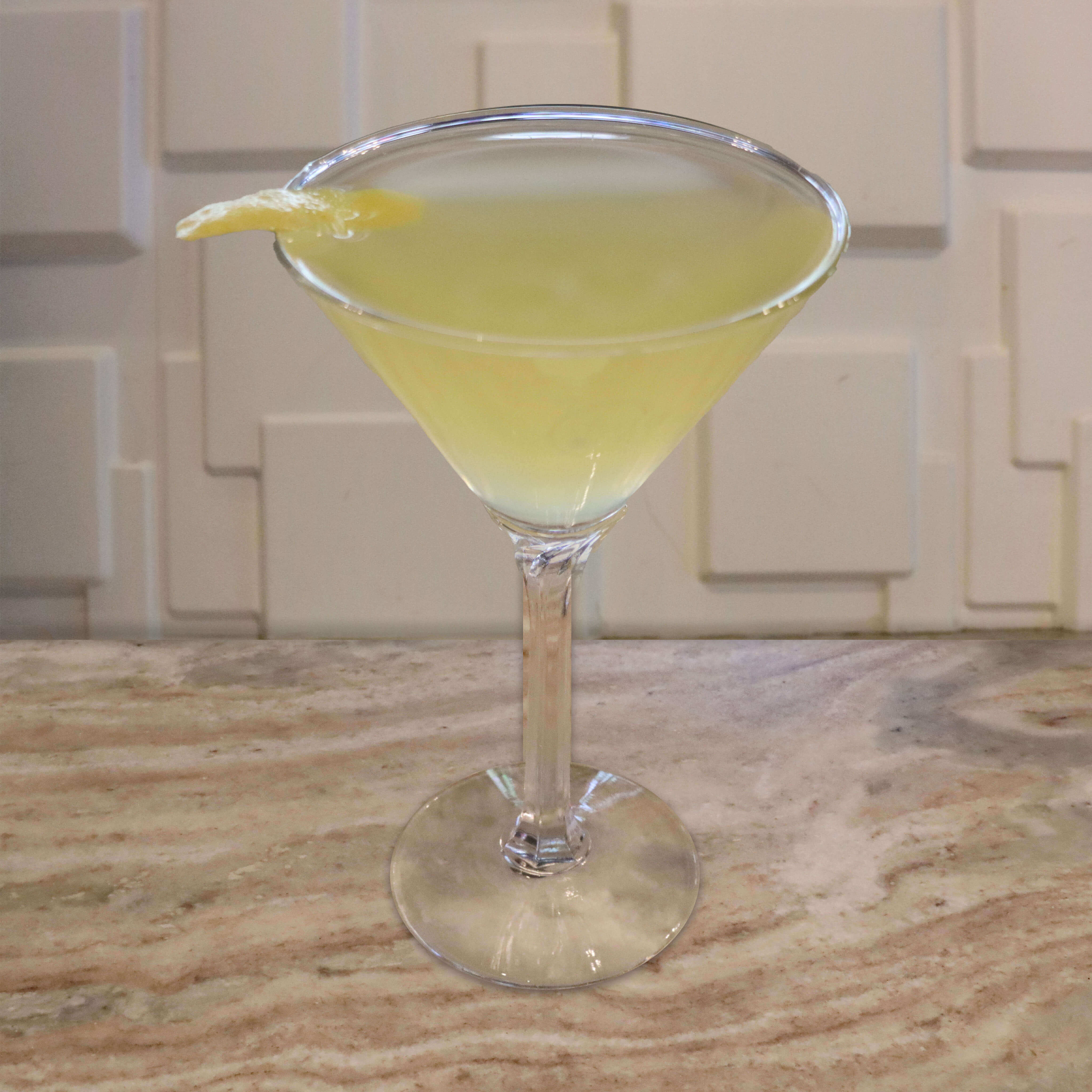 A clear and crisp cocktail garnished with a thin lemon twist.
