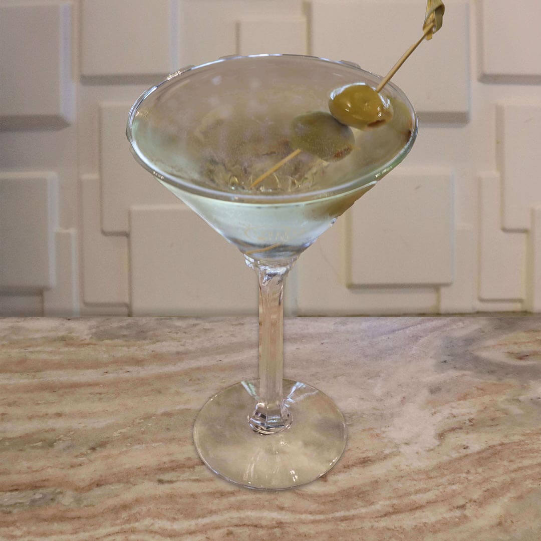 A clear cocktail garnished with a green olive on a pick.