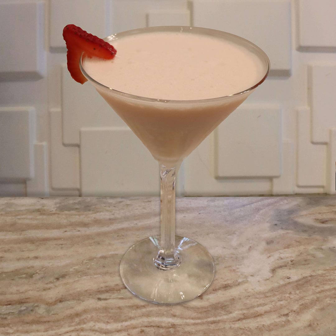 A creamy, pale pink strawberry cocktail served in a glass, garnished with a fresh strawberry slice.