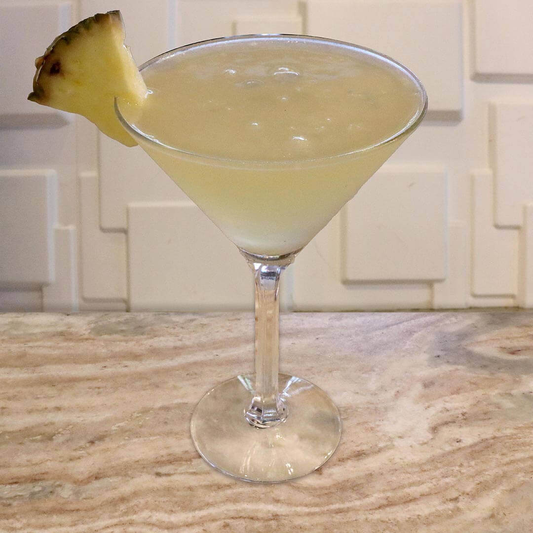 A pale yellow tropical mango cocktail with a fresh pineapple wedge garnish.