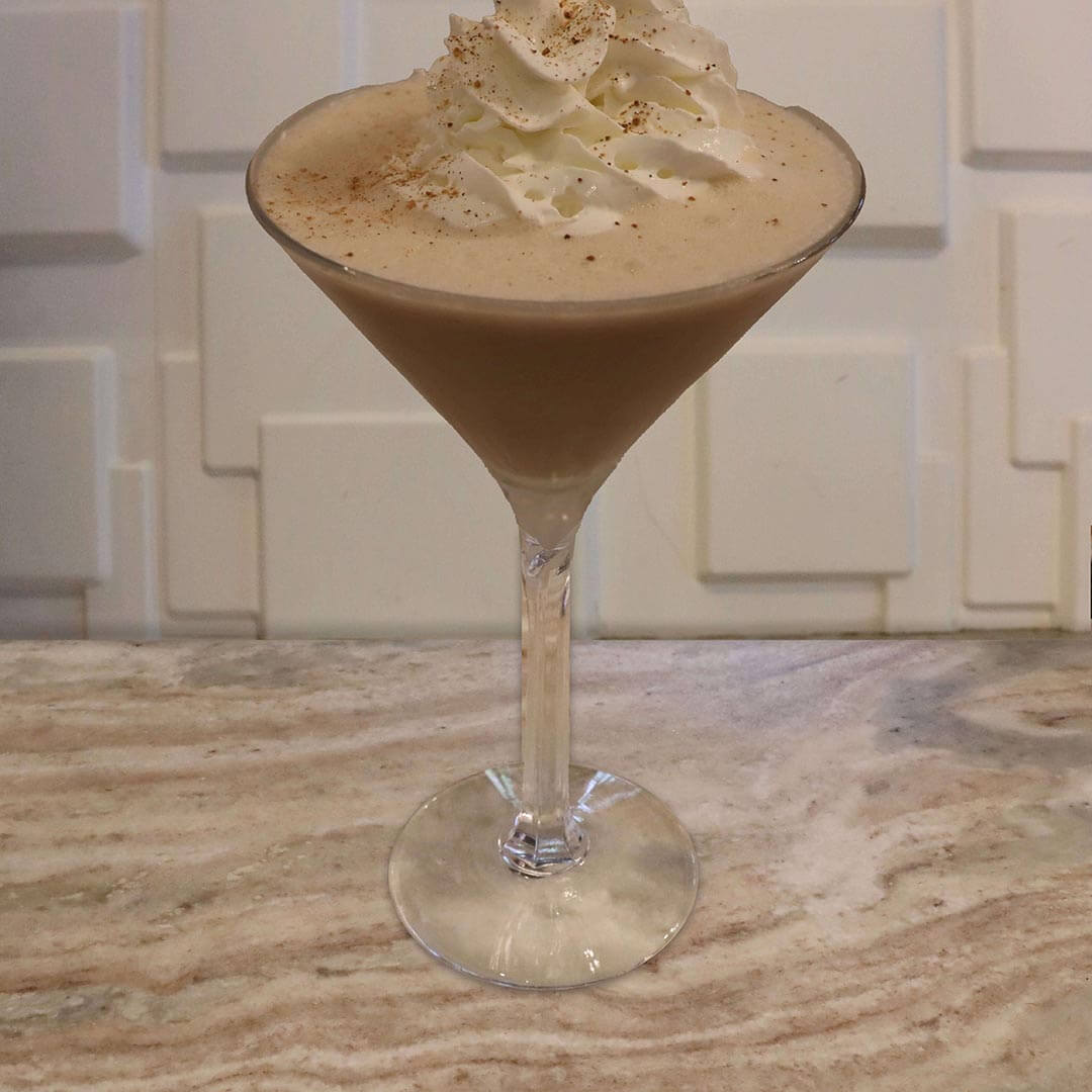 A creamy, light orange-tan cocktail topped with a thick dollop of white whipped cream and dusted nutmeg.