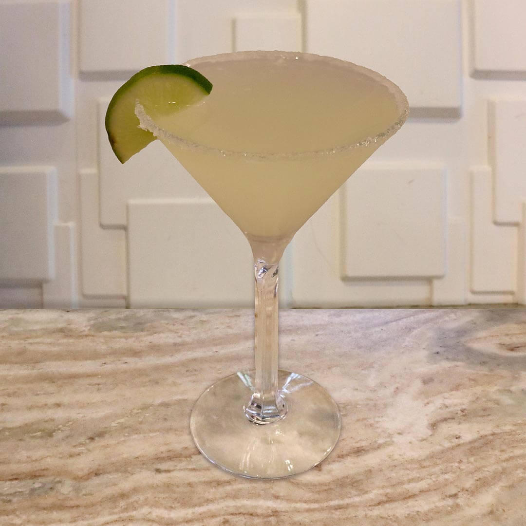 A cloudy, pale green lime cocktail served in a glass with a thick salted rim and a lime slice.
