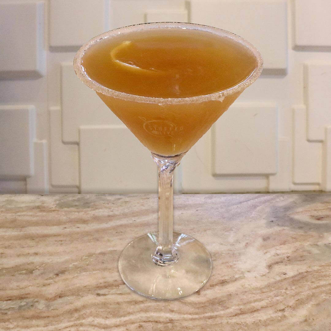 A warm amber cocktail served with a thin lemon twist garnish.