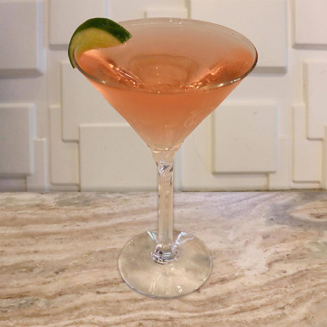 A vibrant, translucent pink cocktail in a chilled glass, garnished with a fresh lime wheel.