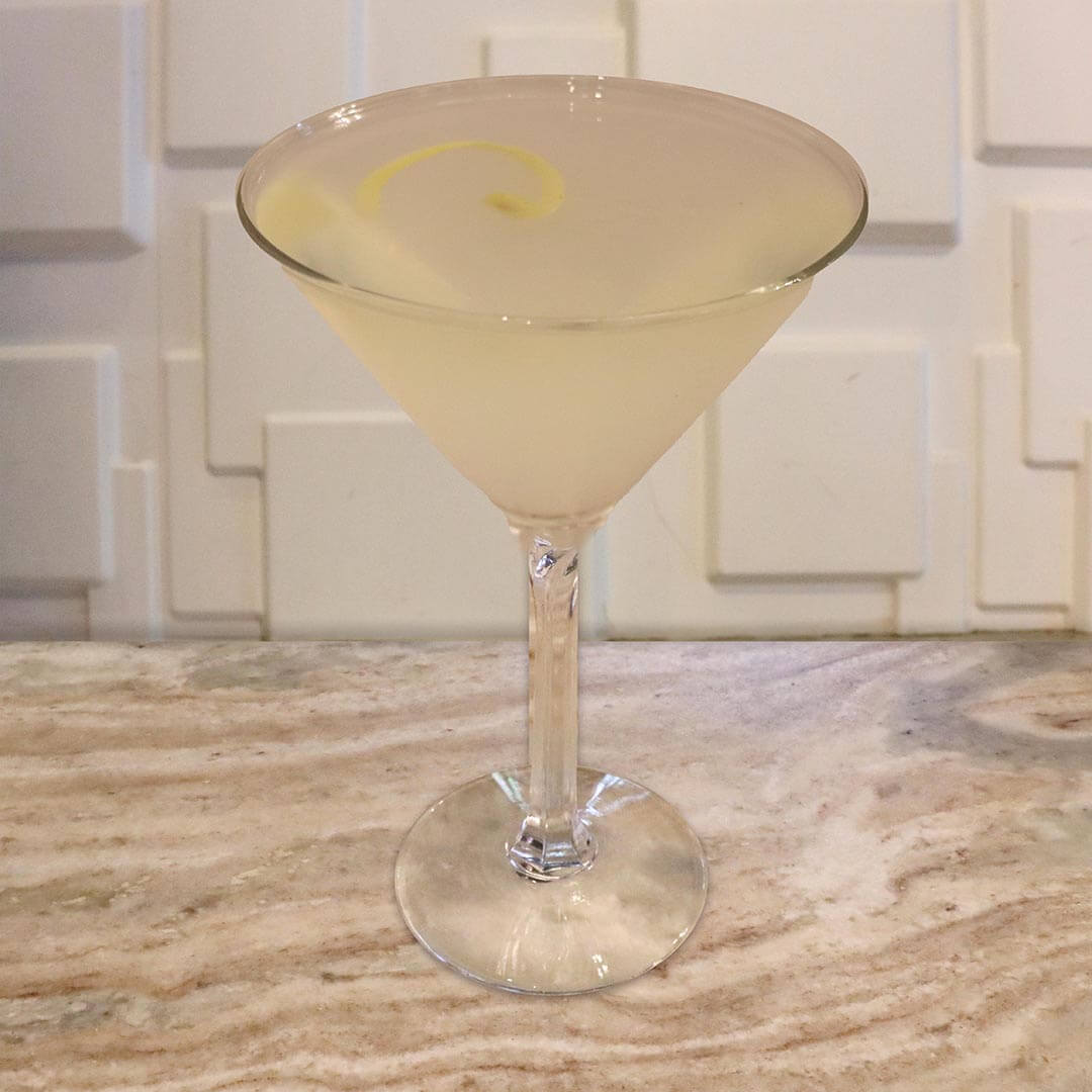 A pale yellow, hazy cocktail served in a chilled glass, garnished with a lemon twist.