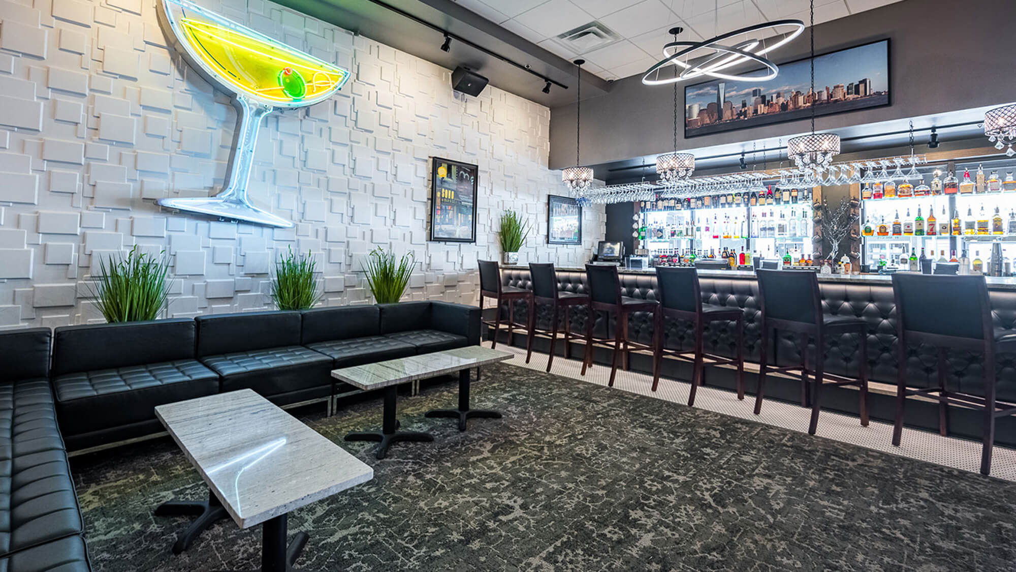 Upscale martini lounge area at The Stuffed Olive in Cedar Falls, Iowa, with black leather sectional seating, marble top tables, and a prominent large neon martini glass sign on a textured white wall.
