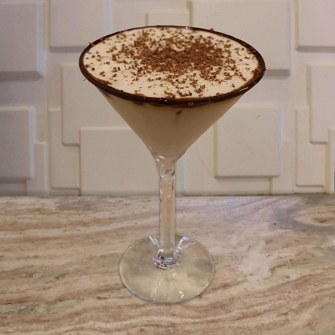A creamy, light brown cocktail with chocolate syrup swirls inside the glass, featuring a thick chocolate rim.