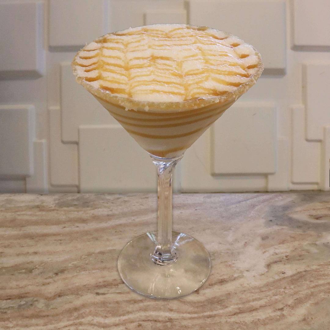 A creamy, light tan caramel cocktail featuring a salted caramel rim and intricate caramel feathering on top.