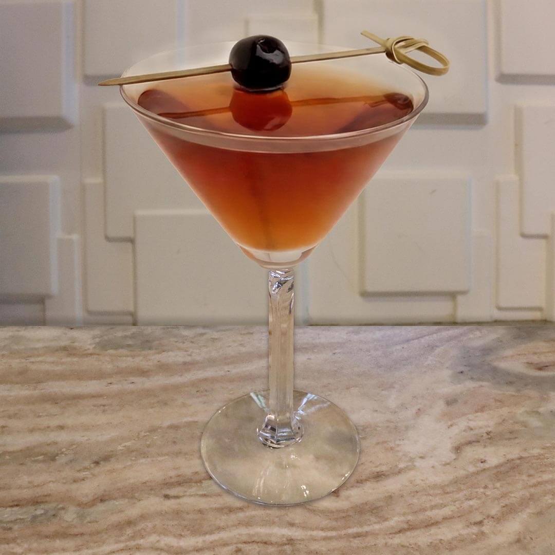 A deep amber, translucent cocktail in a classic glass, garnished with a dark cherry on a wooden pick resting across the rim.