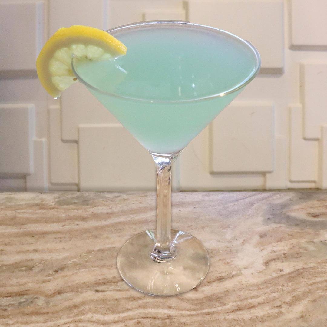 A vibrant, light blue cocktail served in a chilled glass, garnished with a lemon wedge.