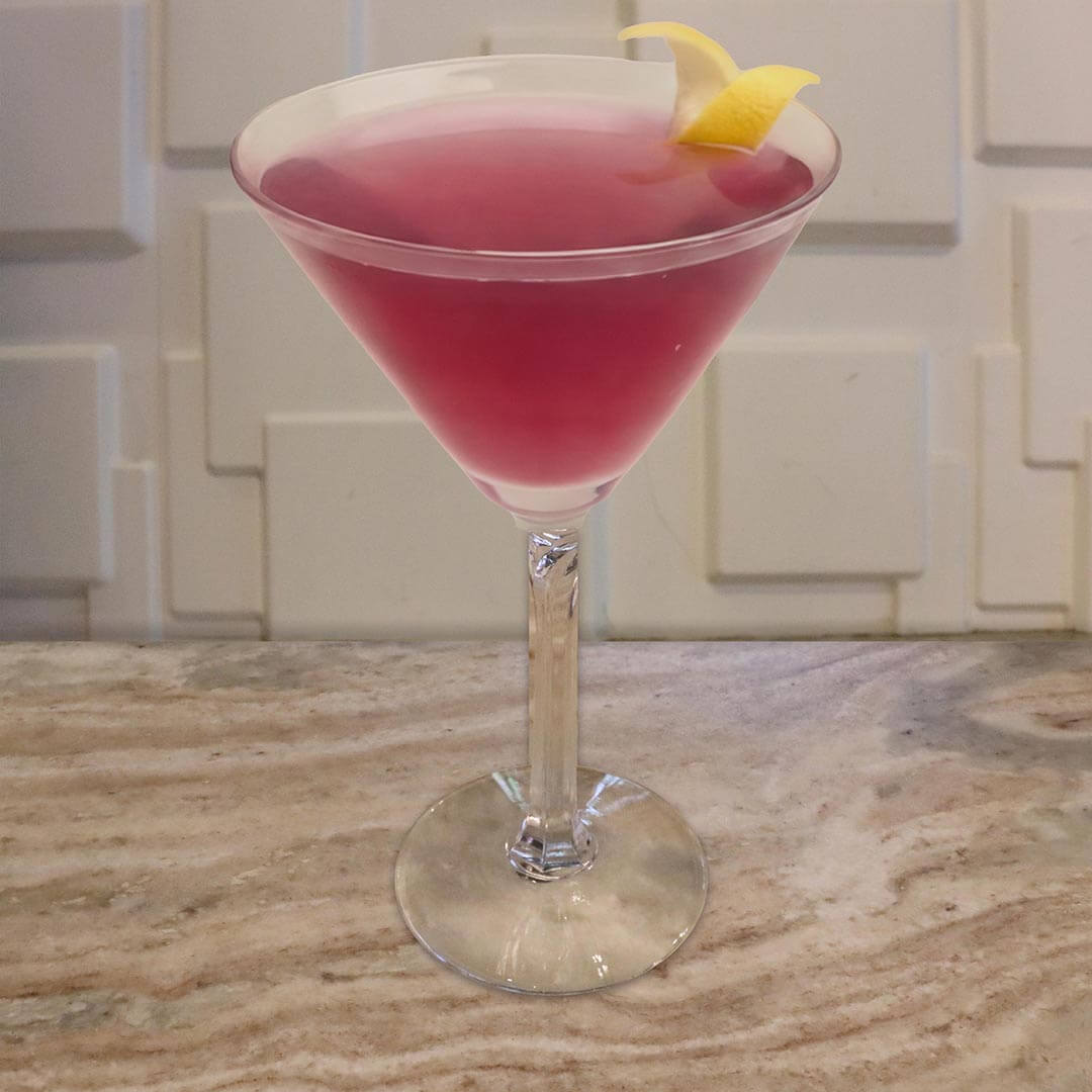 A vibrant magenta-pink cocktail served in a classic glass, elegantly garnished with a thick yellow lemon twist on the rim.