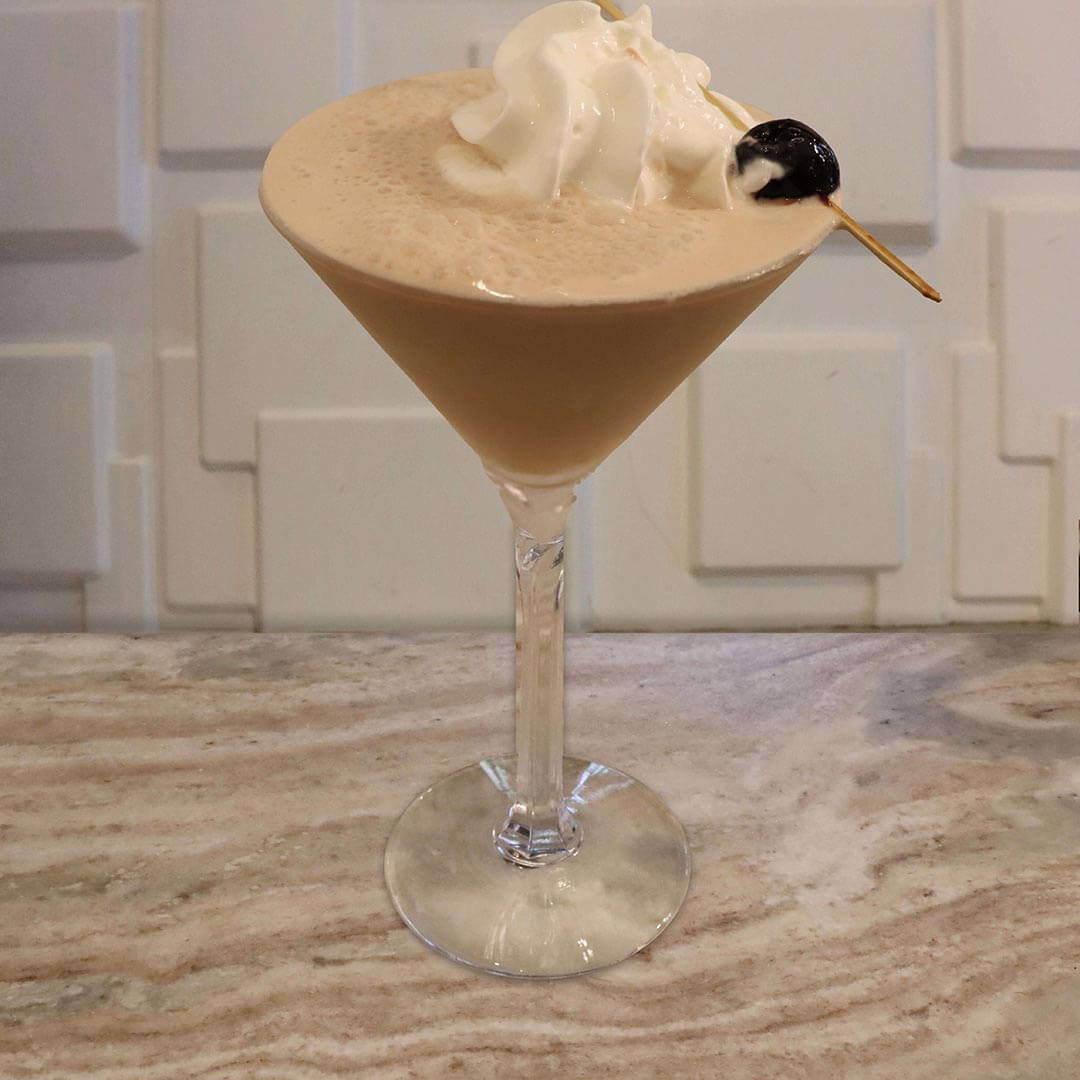 A creamy cocktail topped with whipped cream and a dark cherry.