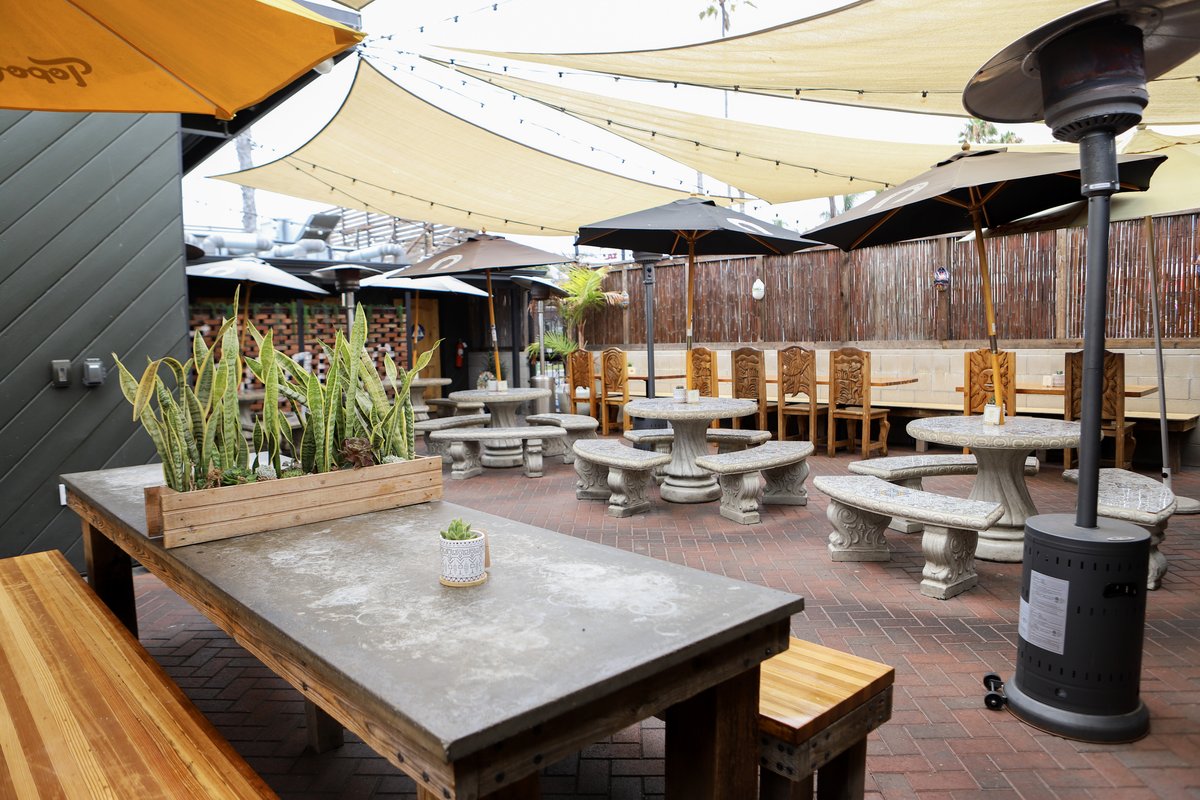 A cozy patio with tables and umbrellas, all situated under a shade cloth, providing a pleasant outdoor dining experience