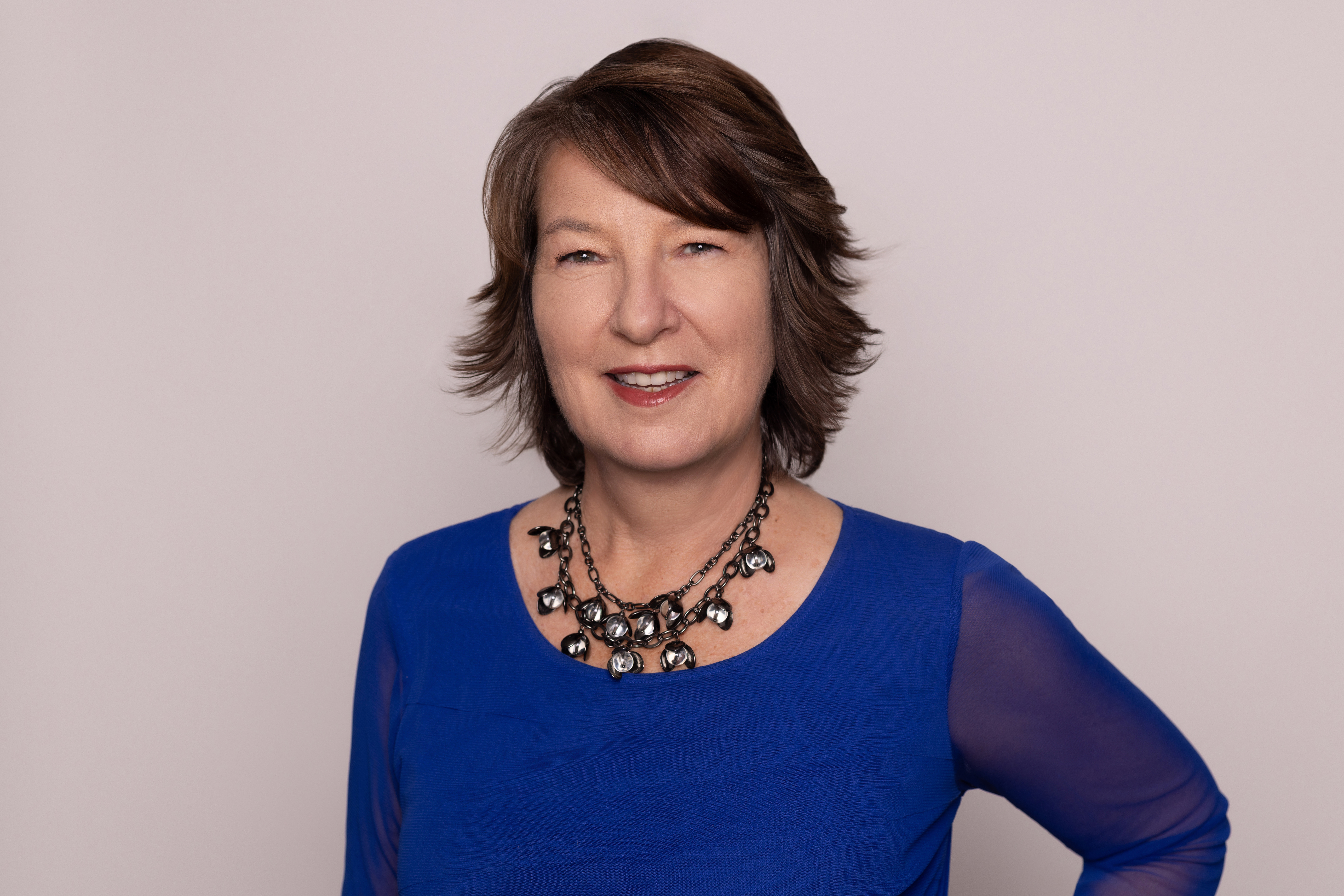 A woman with short, brown hair wearing a blue shirt and necklace.