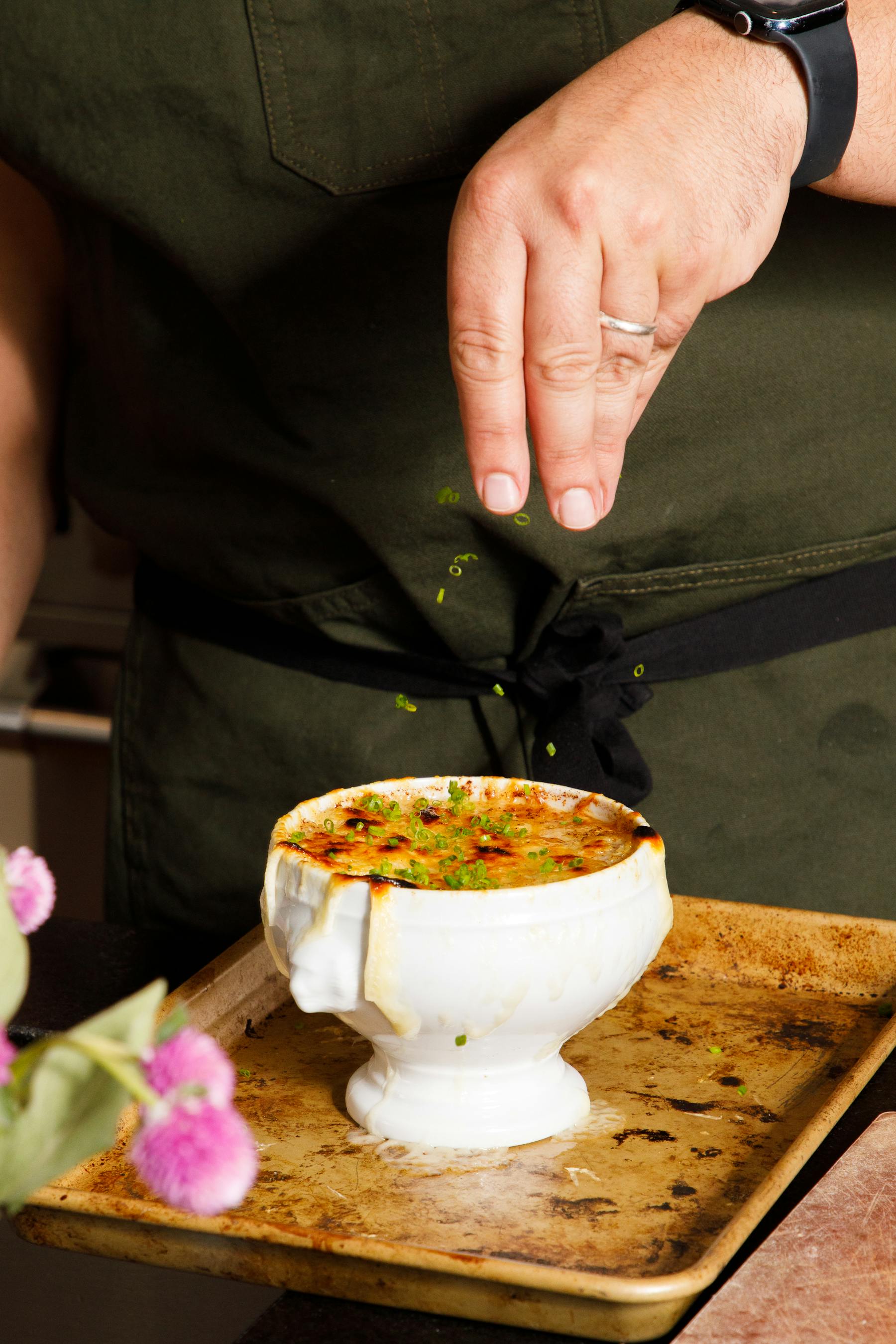 a man sprinkling chives on french onion soup
