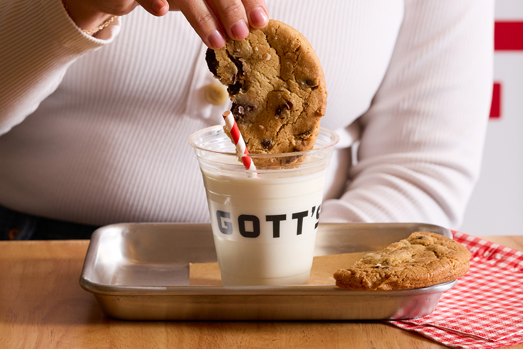a person dipping a chocolate chip cookie into a Gott's cup of milk