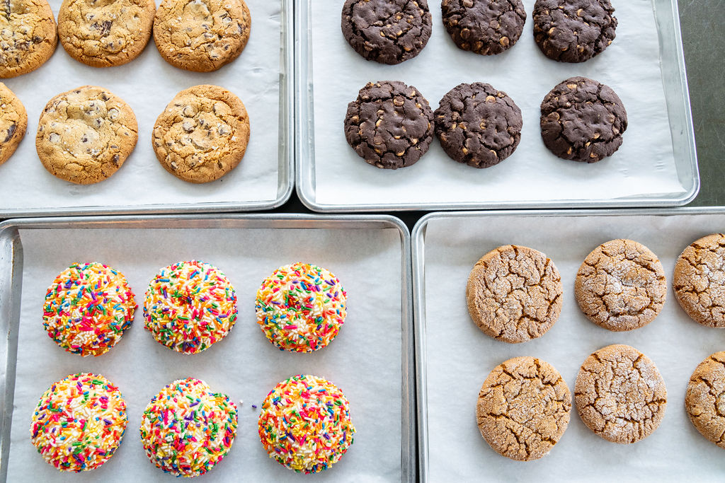 four baking sheets with colorful cookies
