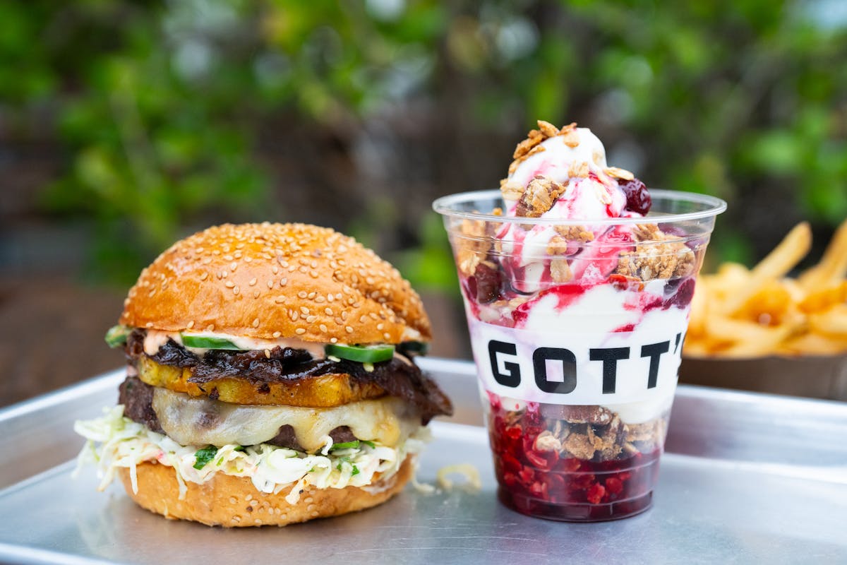a Gott's grilled pineapple burger sitting next to a cherry cobbler parfait