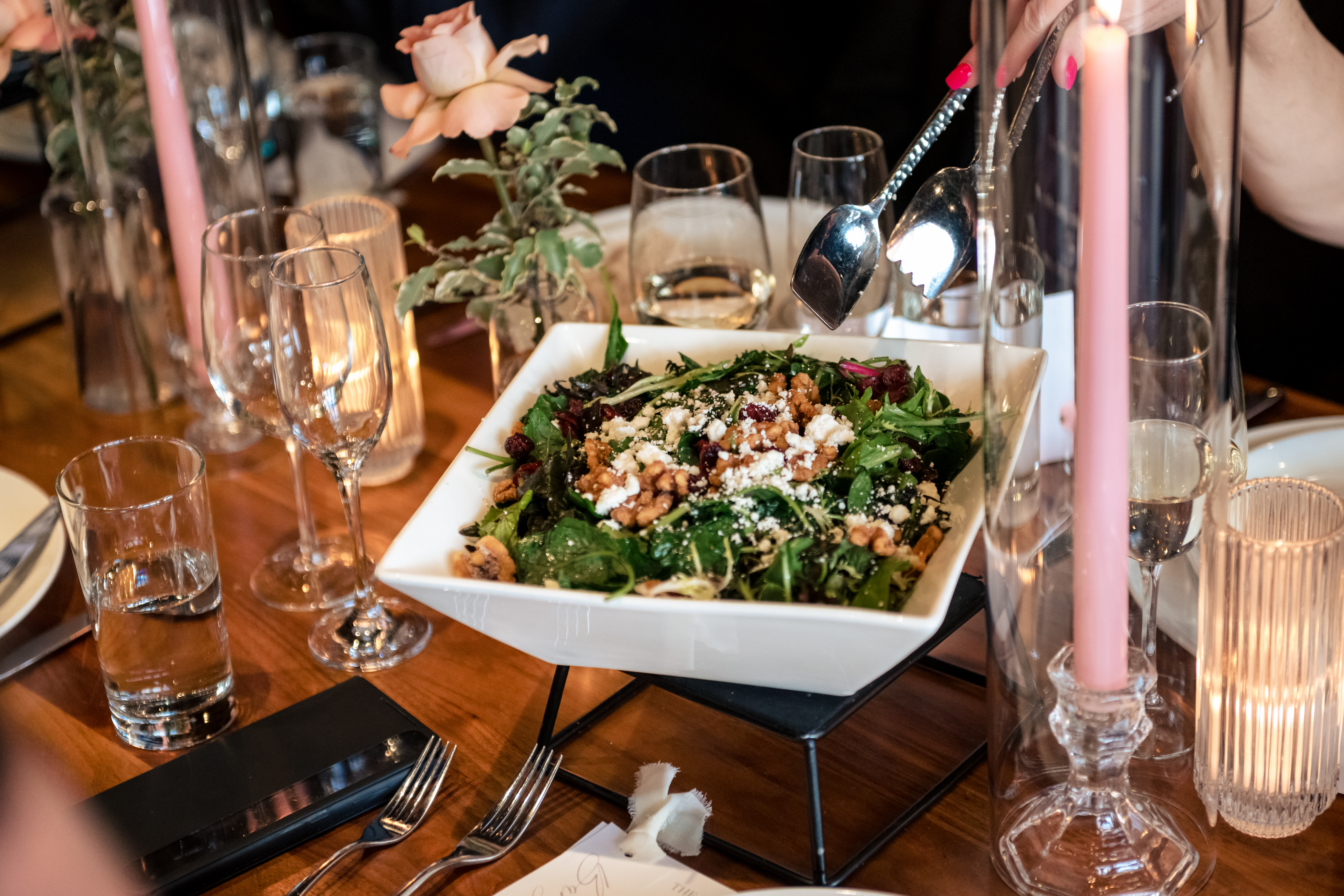 a close up of a banquet style salad made with fresh greens and topped with chickpeas and feta cheese. the salad is surrounded by candles and wine glasses