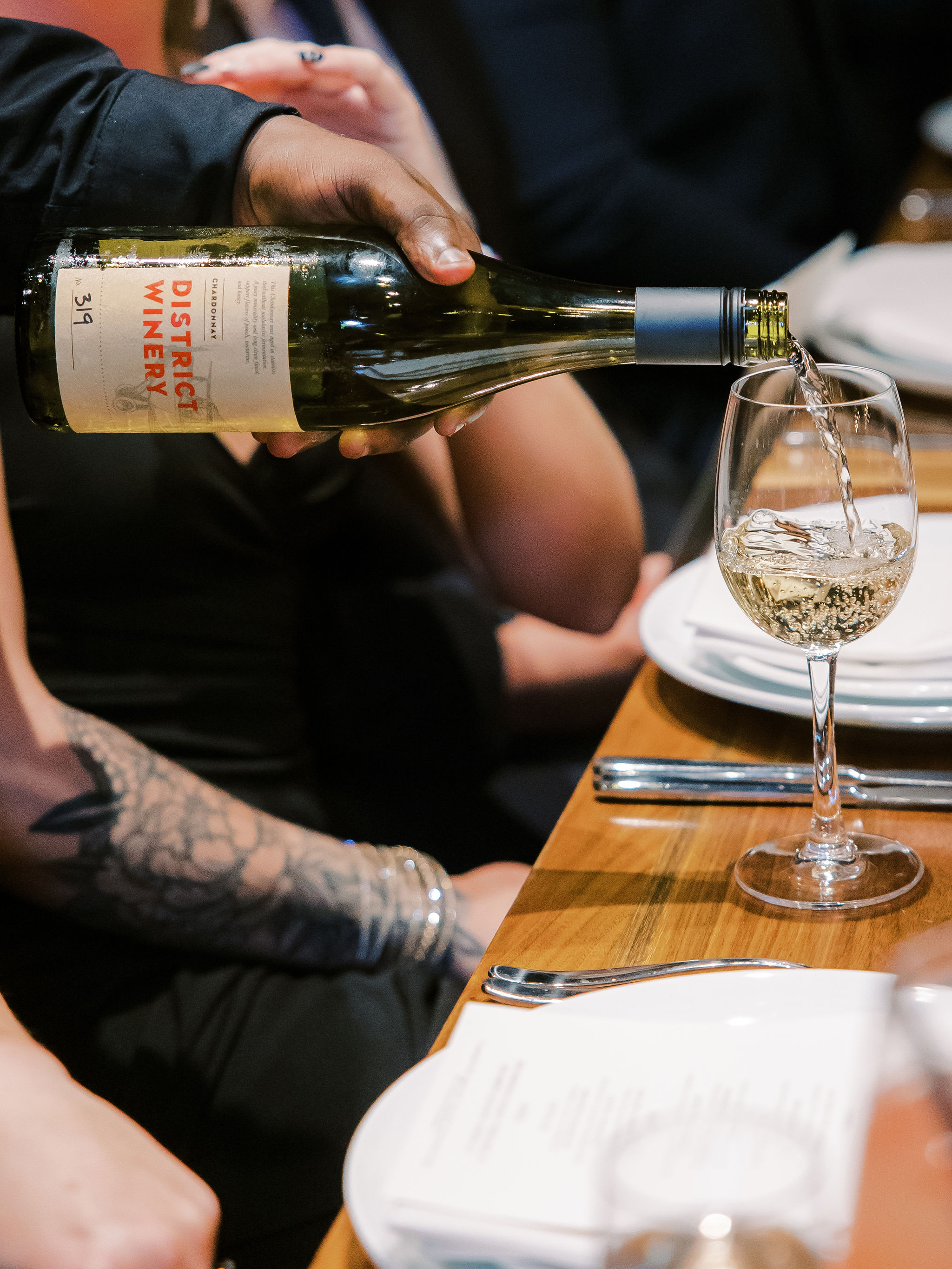 a waiter pours a glass of white wine from District Winery into the glass of a guest sitting at a table