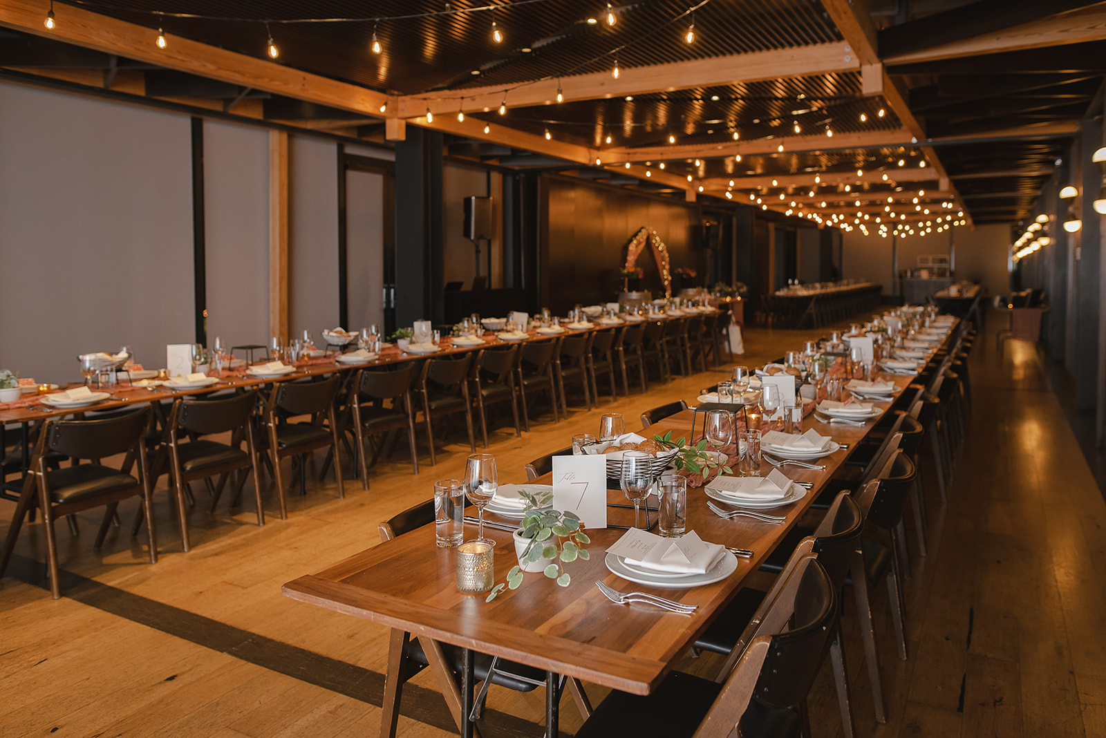 two very long table are set for a wedding banquet at District Winery. The tables stretch the entire space and can seat 200 guests. In front of each place setting there is a candle and greenery