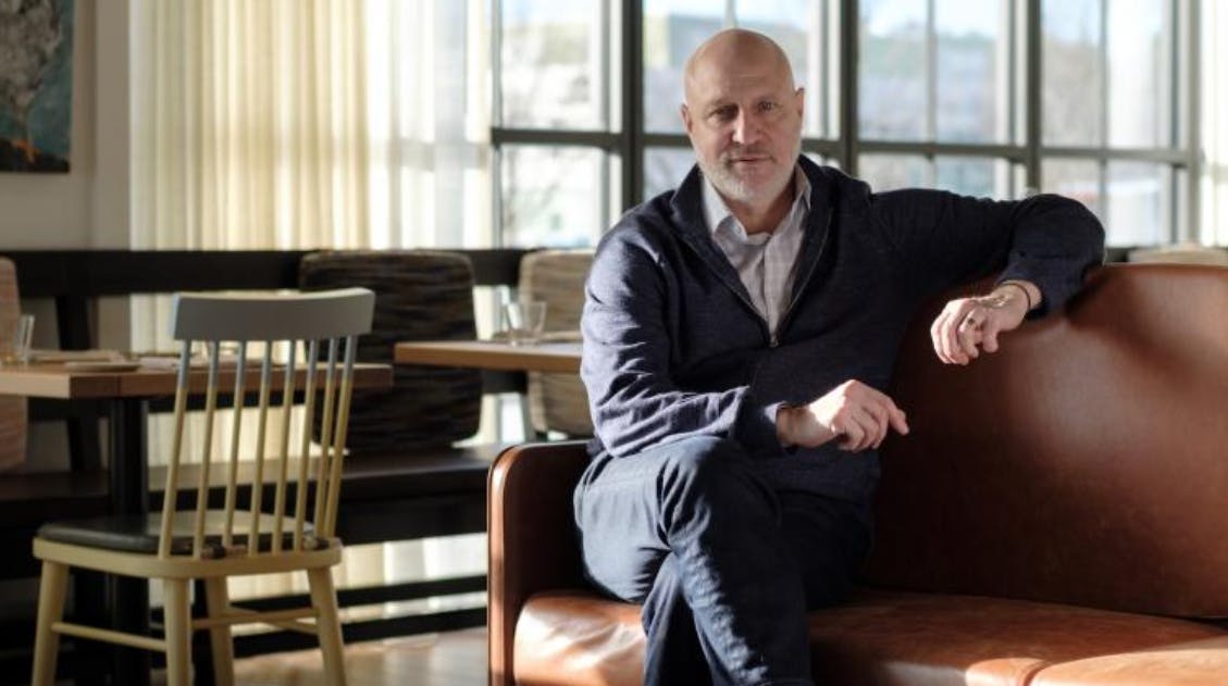 Tom Colicchio sitting on a chair in front of a window