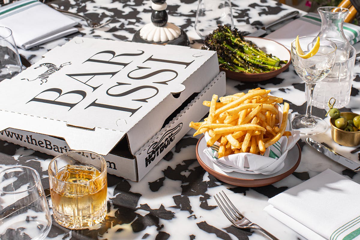 a pizza box on a table with french fries and brocollini