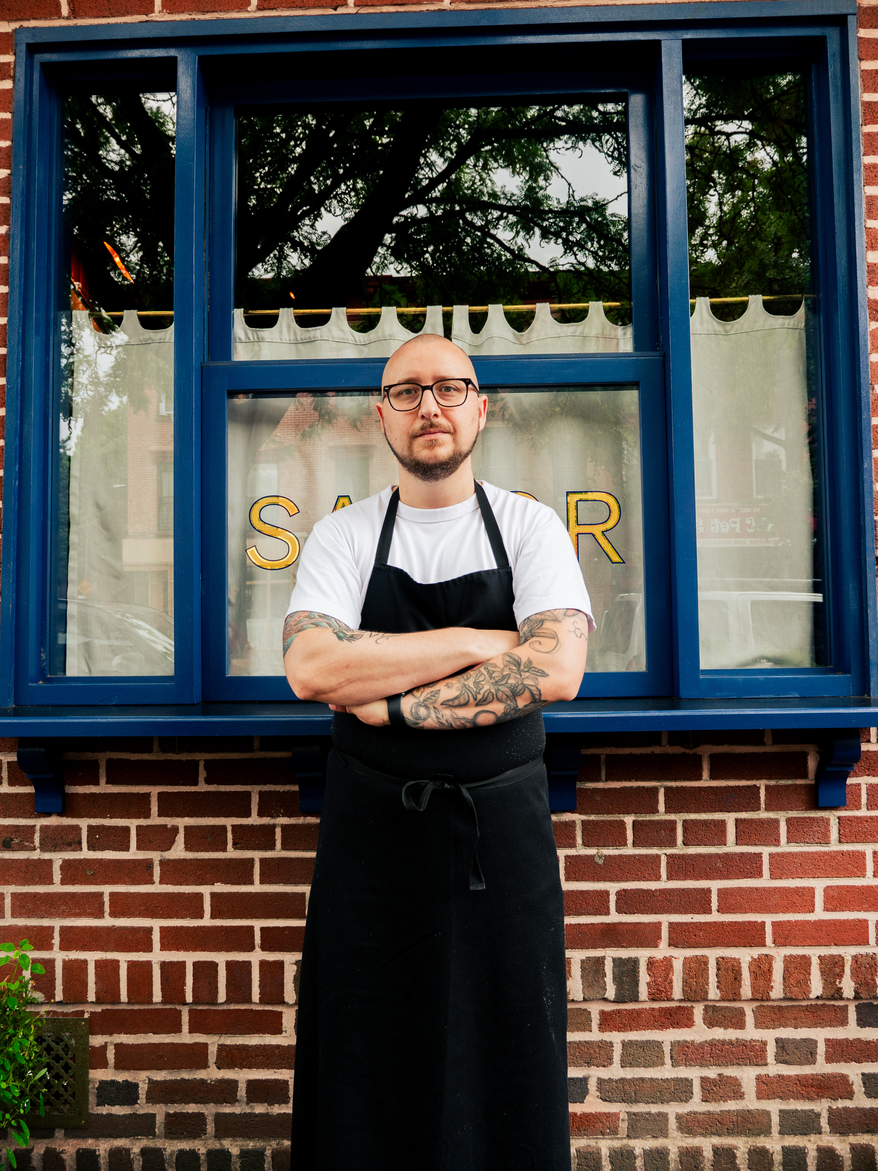 a man wearing a black apron standing in front of a brick building