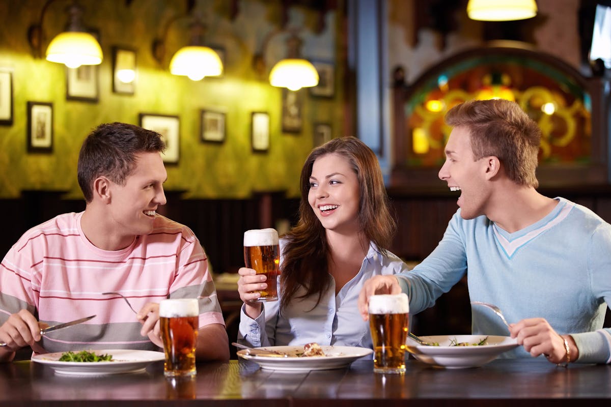 three people sitting down at a table drinking beer