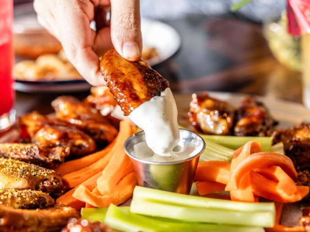 a close up of a person holding a chicken wing being dipped in ranch