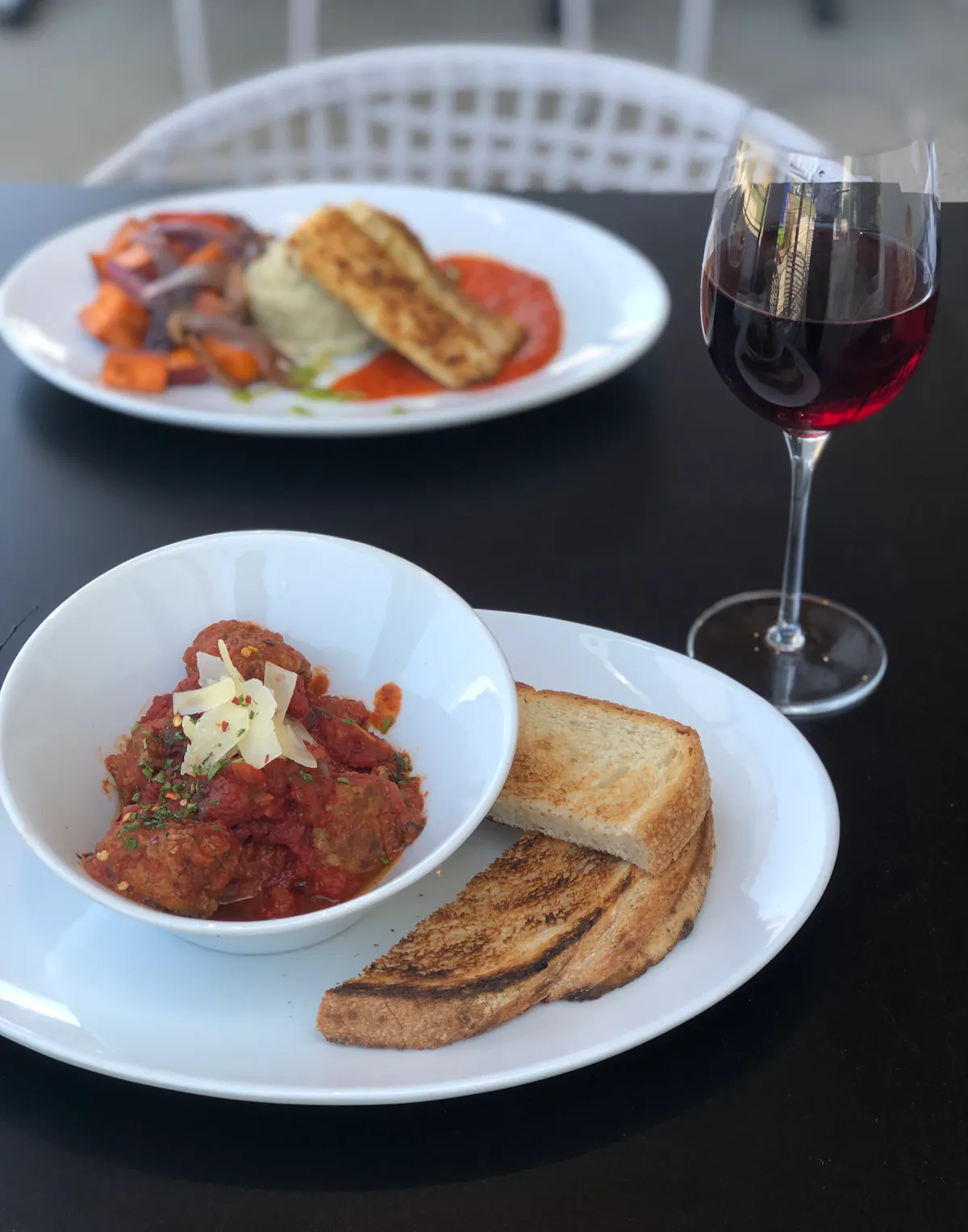 Close up of a white plate topped with Meatballs, Sourdough and Glass of wine