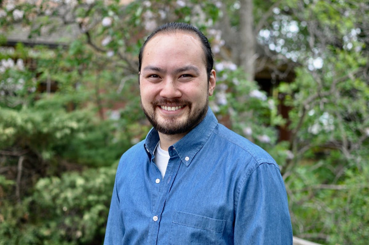 a man wearing a blue shirt standing in front of a tree