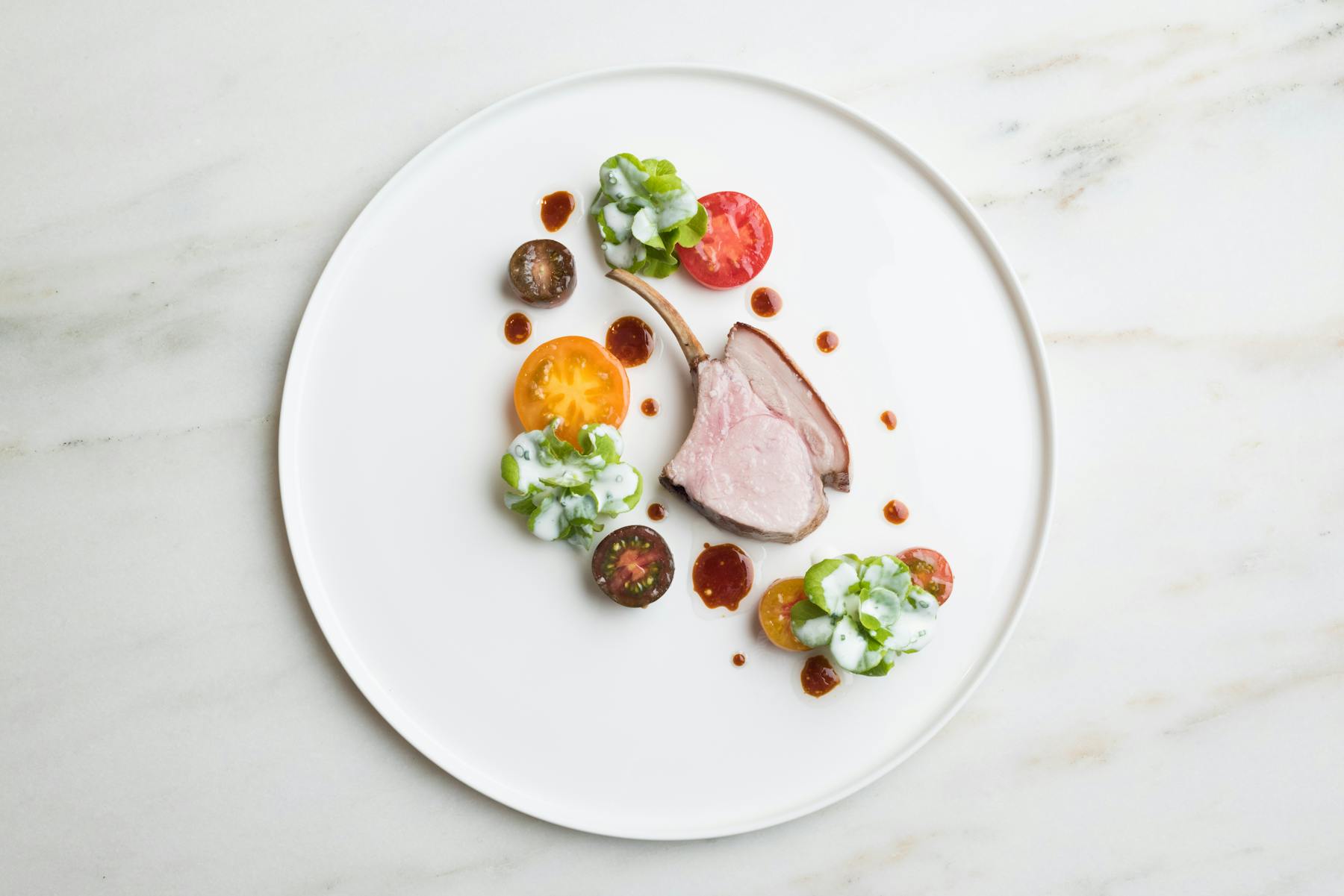 lamb chops served on a white plate with tomatoes