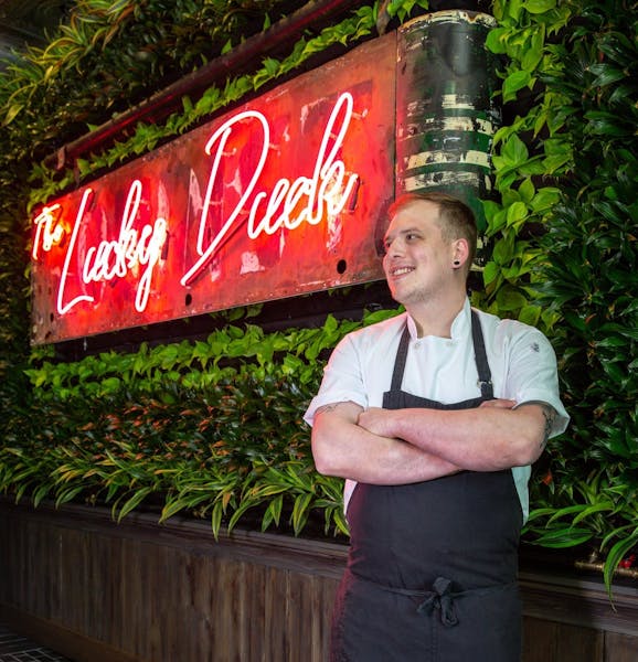 a man standing in front of a restaurant sign with his arms crossed