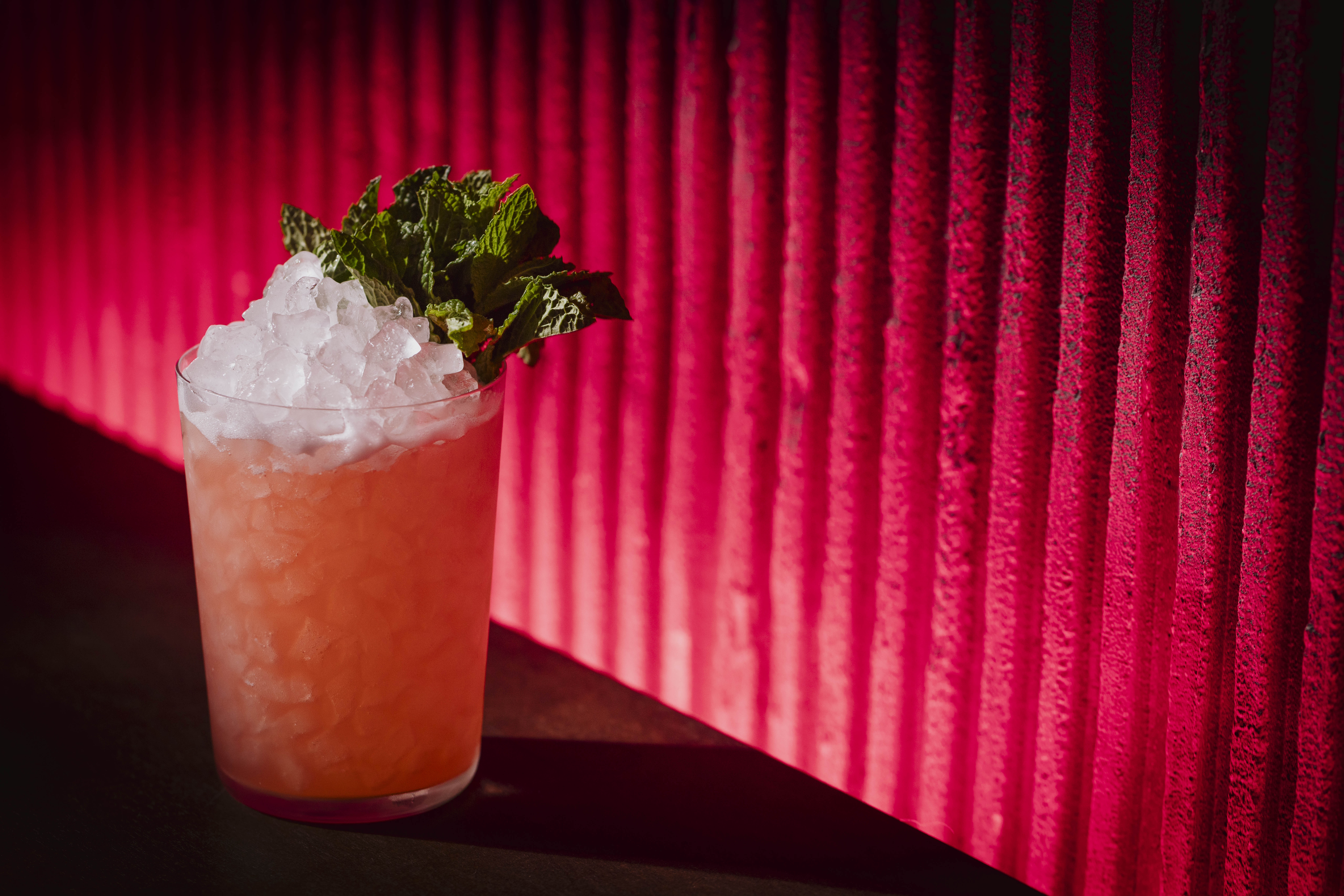 a glass of pink drink with ice and mint leaves