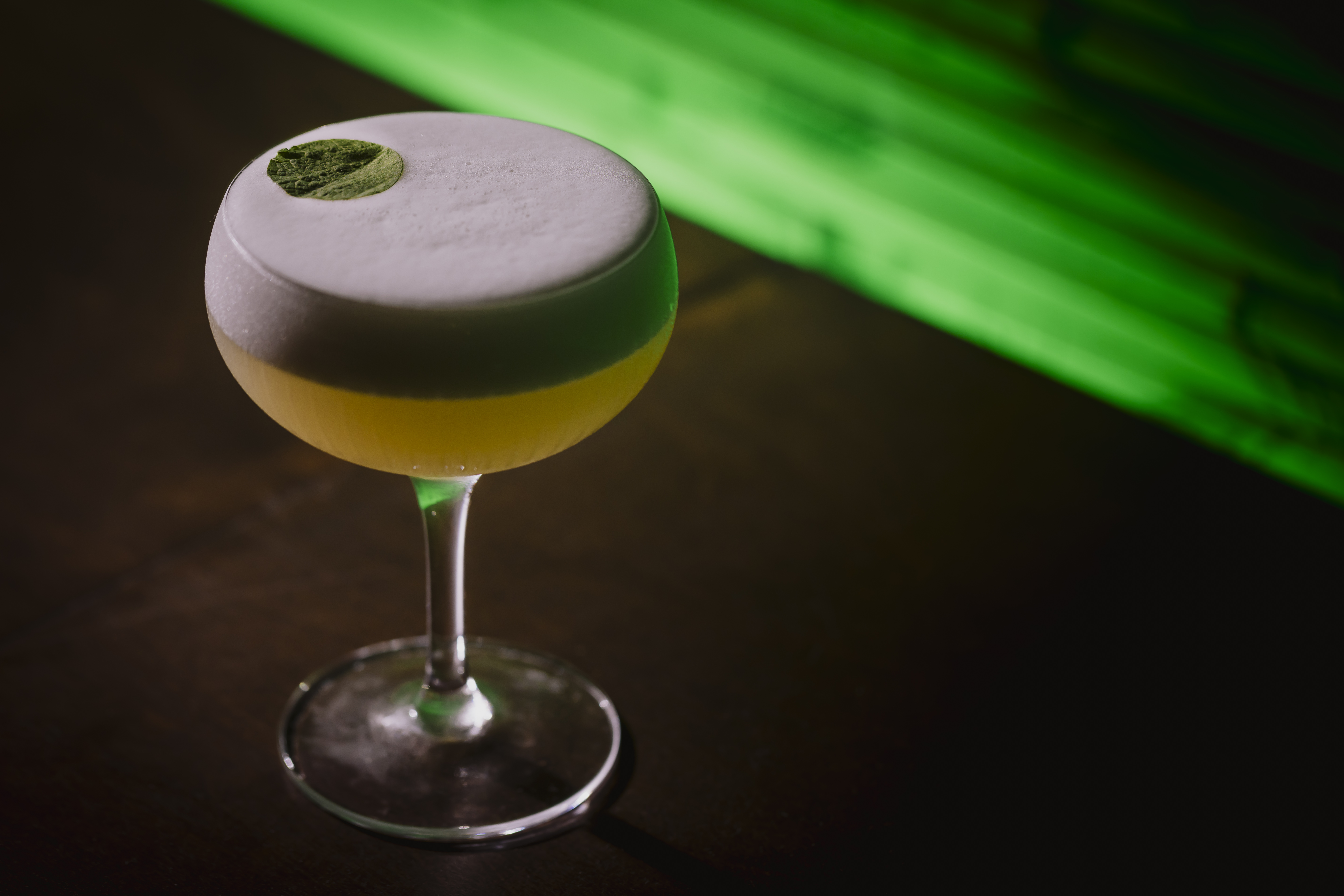 a glass with a yellow drink with a green leaf on top