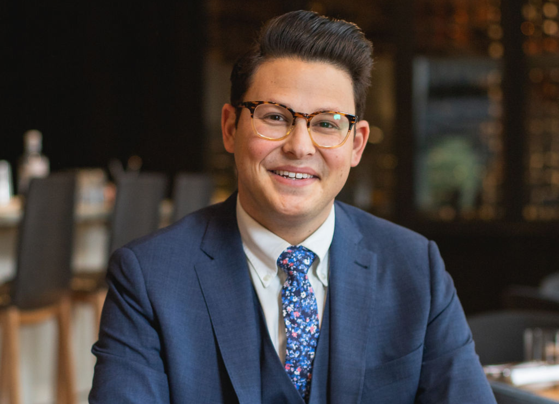 a man wearing a suit and tie smiling at the camera