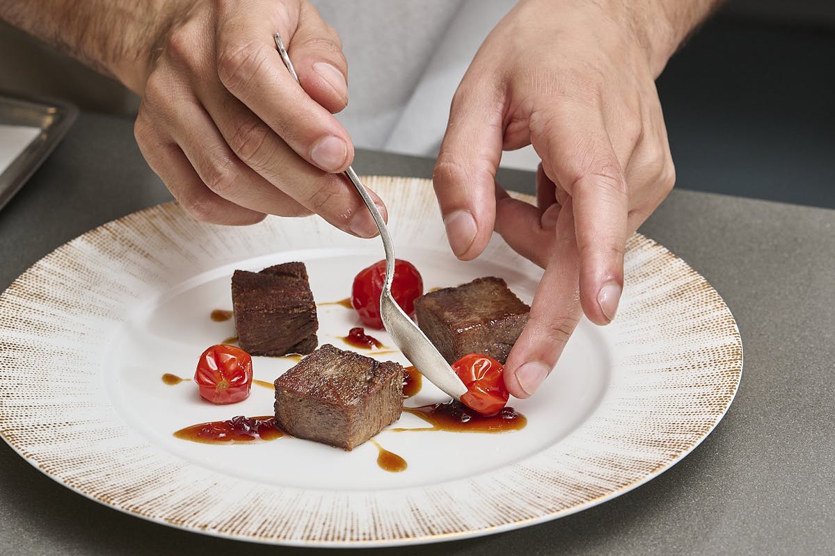 chef plating a dish with wagyu tongue and sweet 100 tomatoes