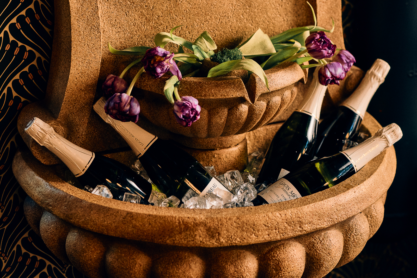A photo of wine bottles in a fountain with some tulips.