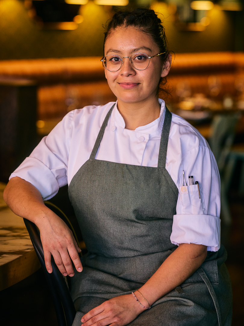 a woman wearing an apron and sitting at a bar