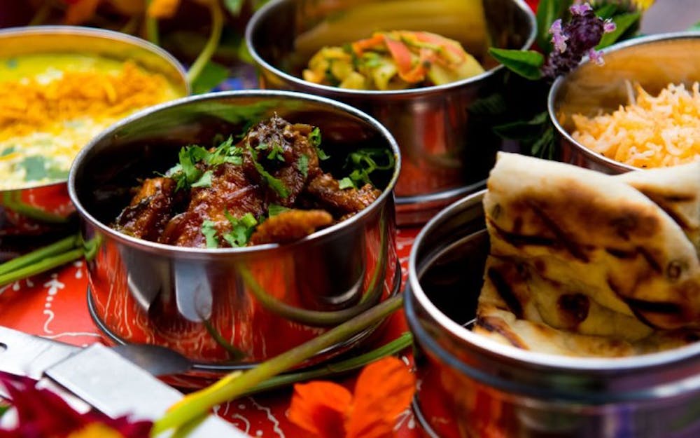 a variety of flavorful curries, tender roasted meats, and vibrant spices, served in tins representing the rich culinary heritage of Indian cuisine