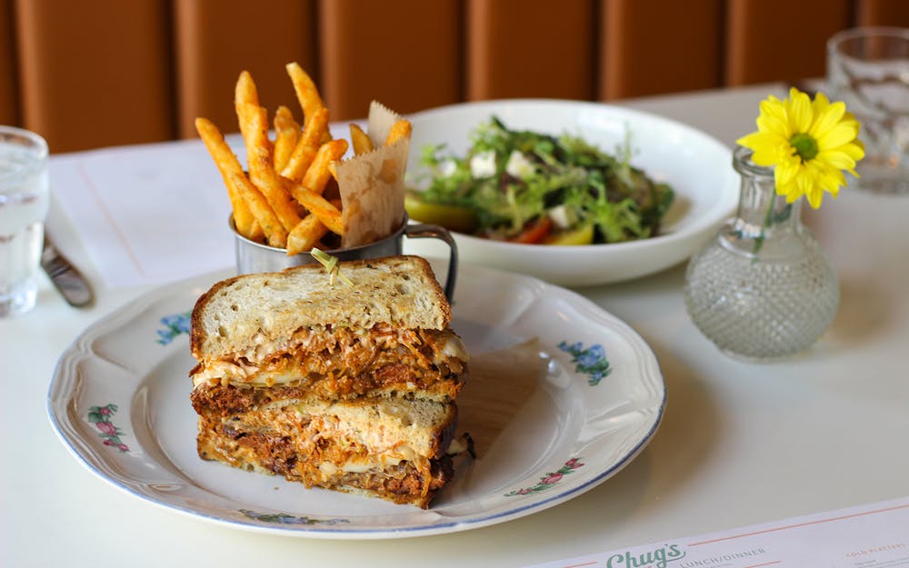 A mouthwatering Chug's Frita Patty Melt served with a side salad and crispy French fries, a delectable combination of comfort food delights