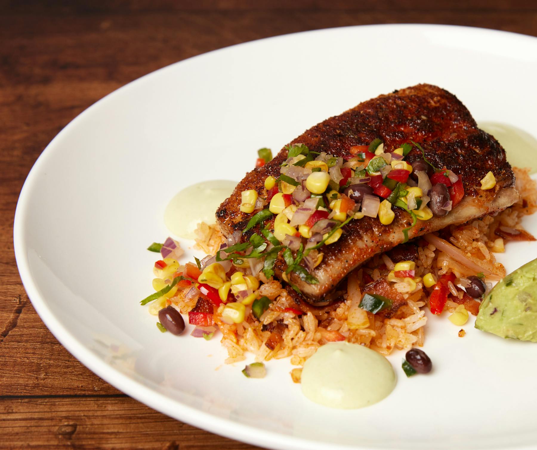 Seasoned fish fillet on rice and vegetables, topped with corn and black bean salsa, avocado, and green sauce.