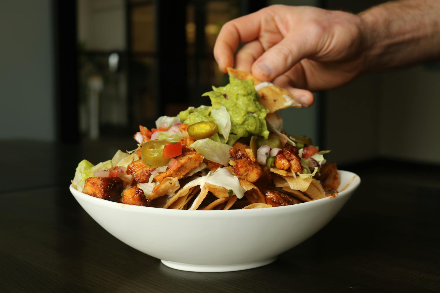 A hand dipping chips into a bowl of nachos